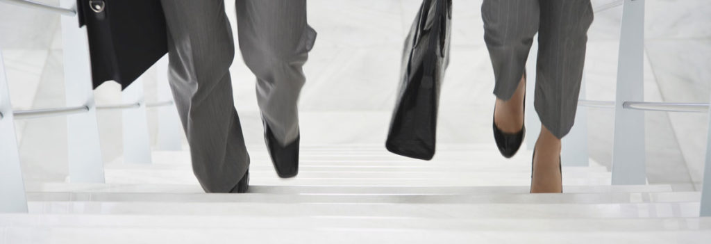 2 Personen laufen eine Treppe hoch. Ein Mann und eine Frau in Business Kleidung. Man sieht nur die Füße