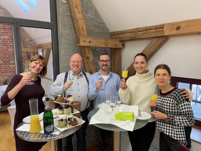 Vier Teilnehmer:innen und die Ausbildungsleiterin stoßen an, auf den erfolgreichen Abschluss der Studi-Azubi-Coach Ausbildung
